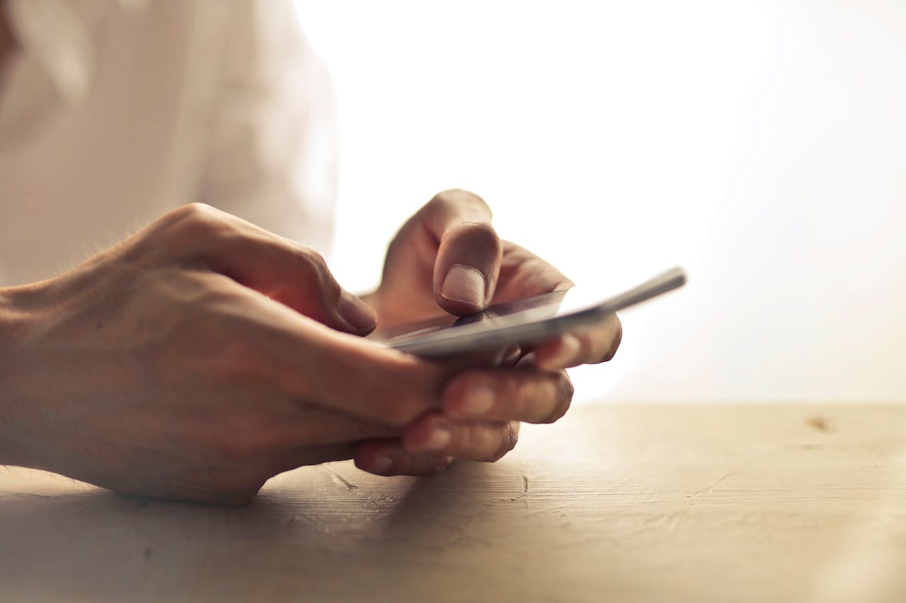 Close-up of an individuals hands holding a smartphone on a table indoors.